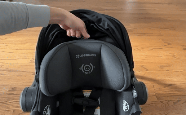 A woman's hand pulls the headrest up and down on a black UPPAbaby Aria infant car seat.