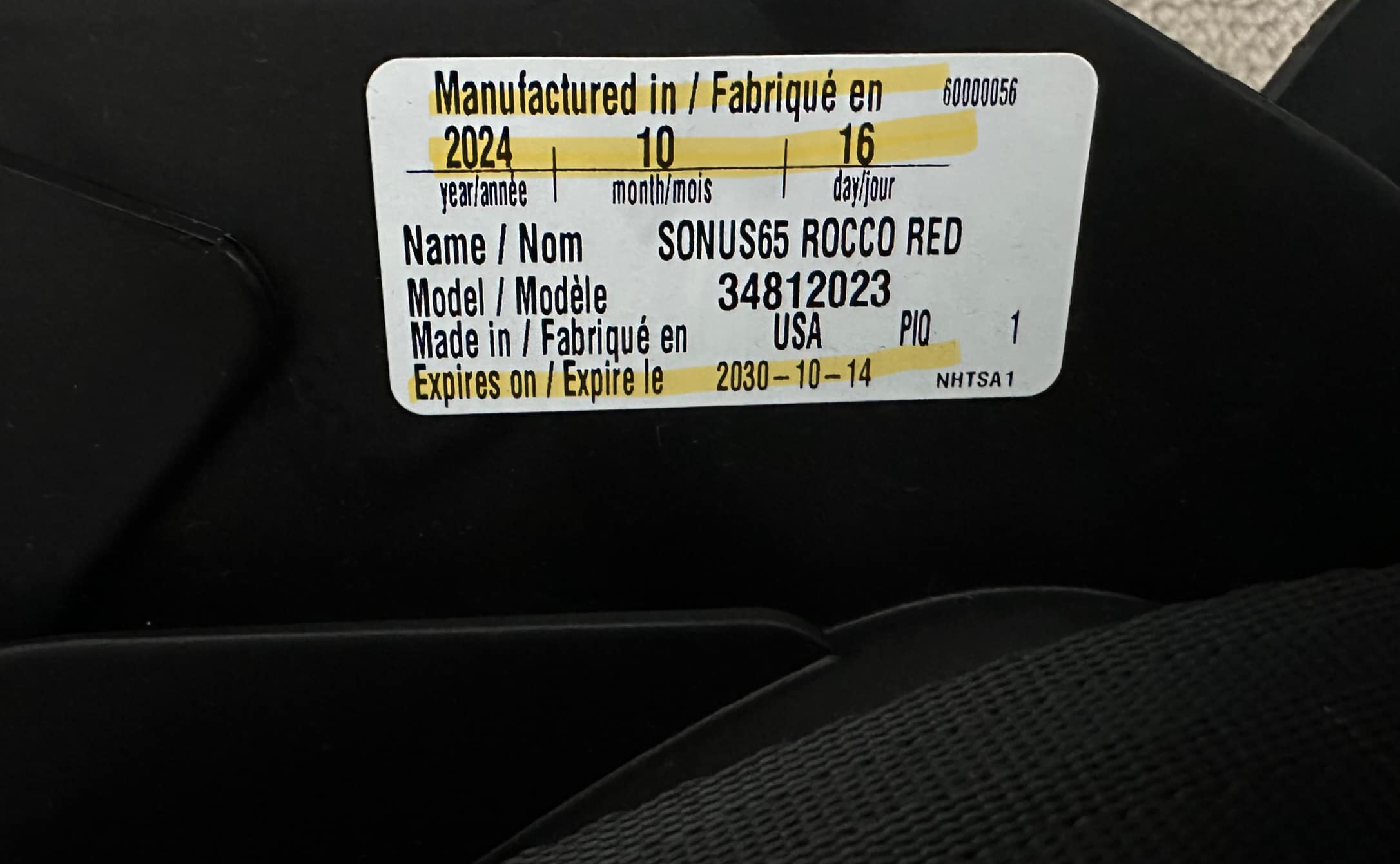 Close-up of a white date of manufacture label on a black car seat shell showing important safety details, including the date of manufacture, expiration date, model name, and number.