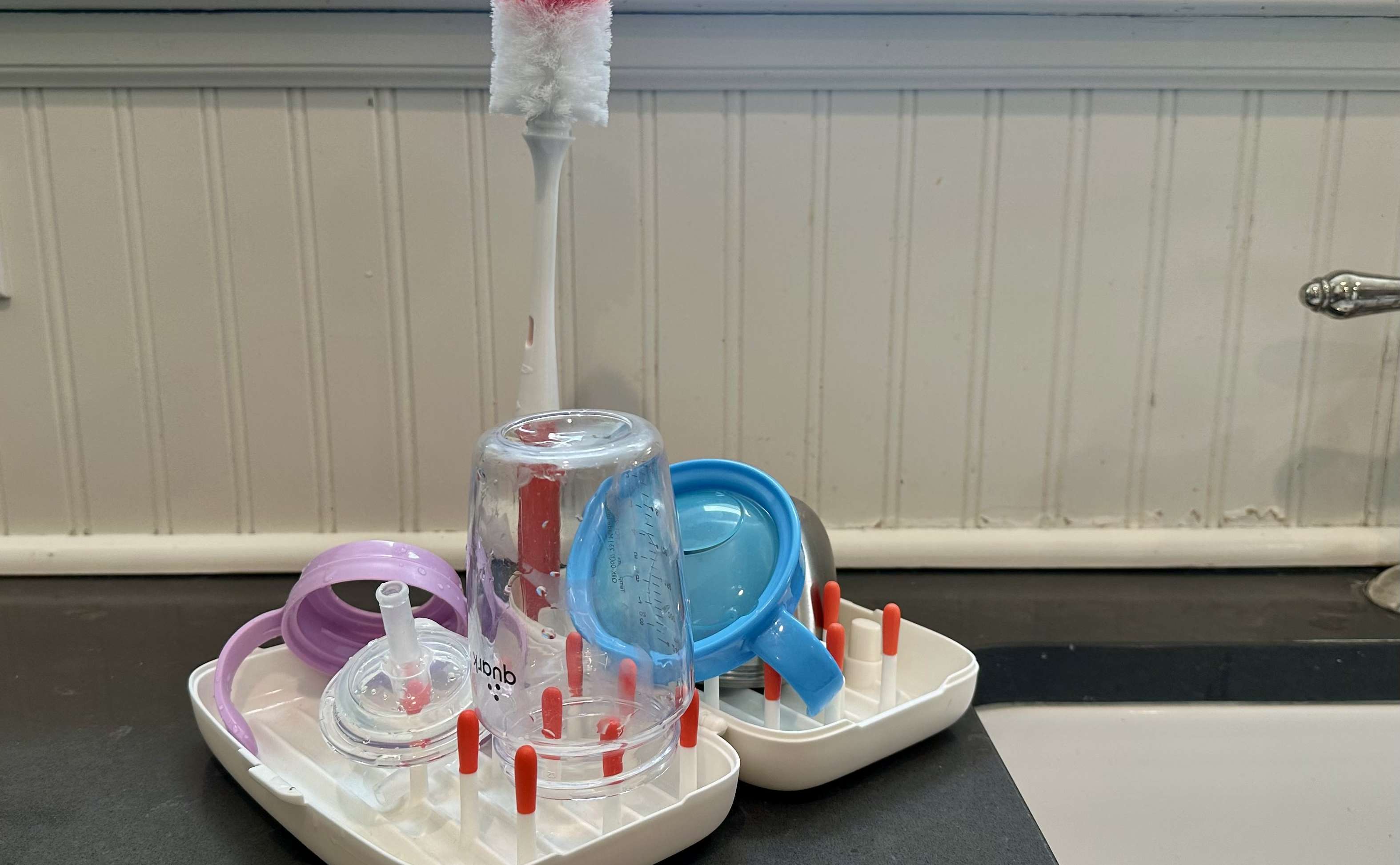 White Oxo On the Go drying rack filled with a straw cup, a snack container and accessories on top of a kitchen counter.