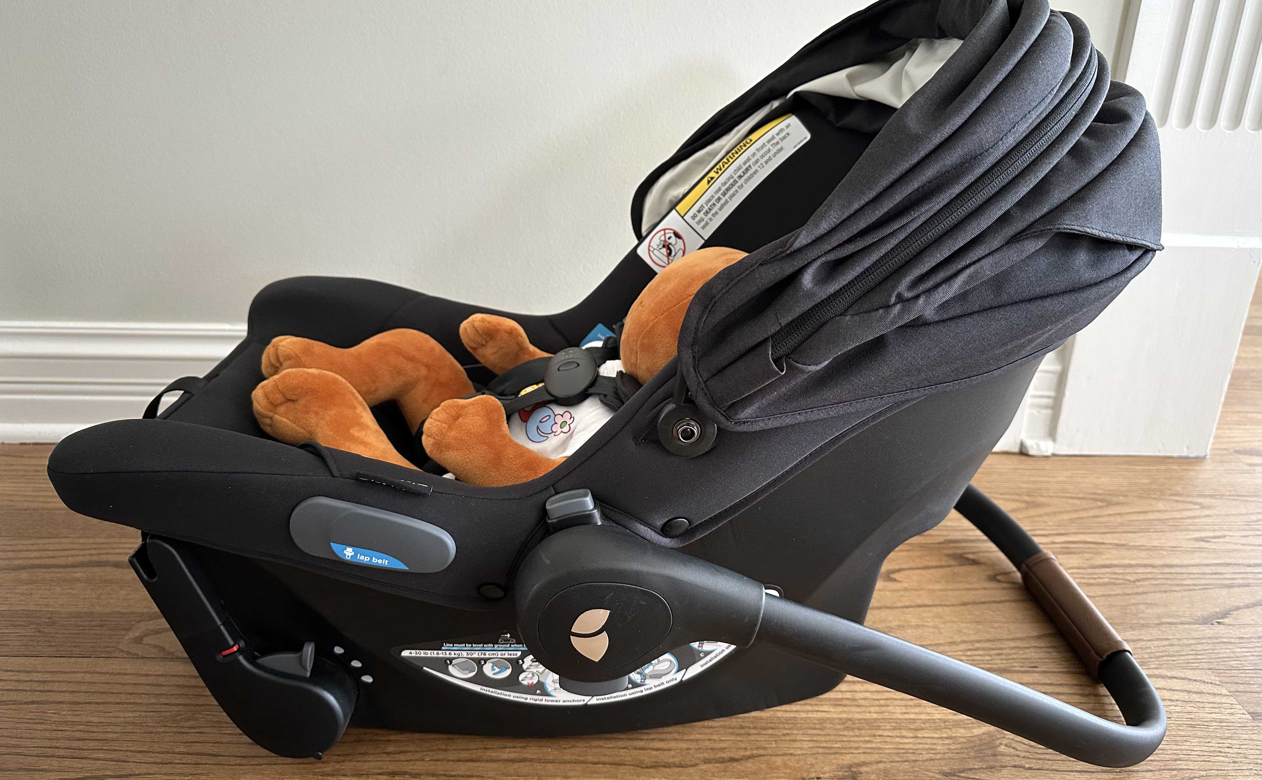 Side view of a small doll harnessed into a Joie Mint Latch Baseless Infant Car Seat in black.