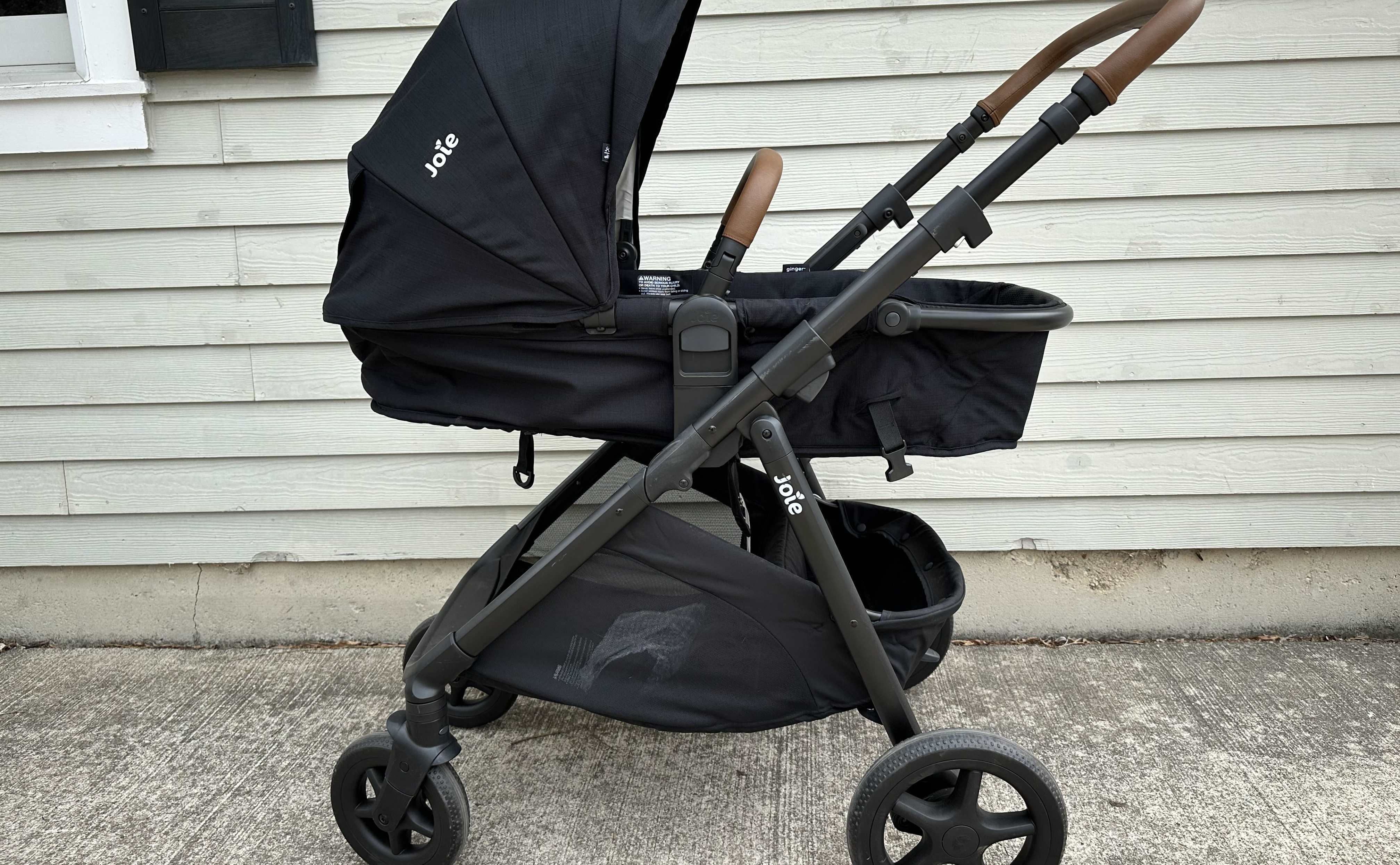 A black Joie Ginger stroller in bassinet mode against a beige background.