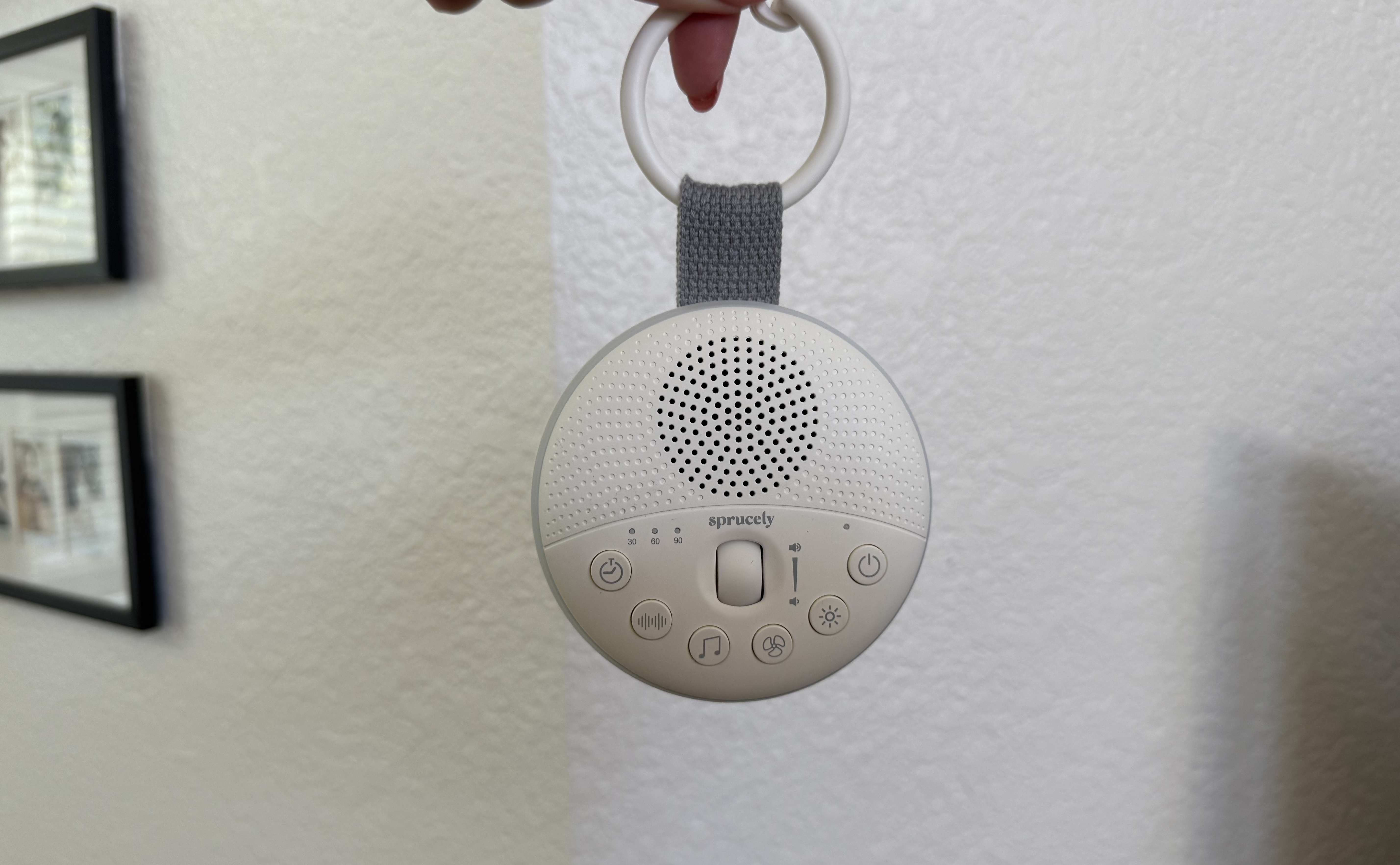 A hand holding the white Sprucely Travel Sound Machine by its detachable hook.