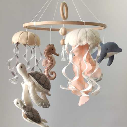 A baby mobile in a nautical boho style for a crib with felt sea creatures: jellyfish, dolphin, turtle, and seahorse in neutral colors.
