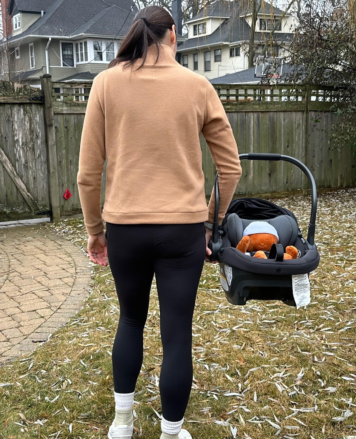A woman with brown hair carrying an UPPAbaby Aria infant car seat using the ergonomic handle.