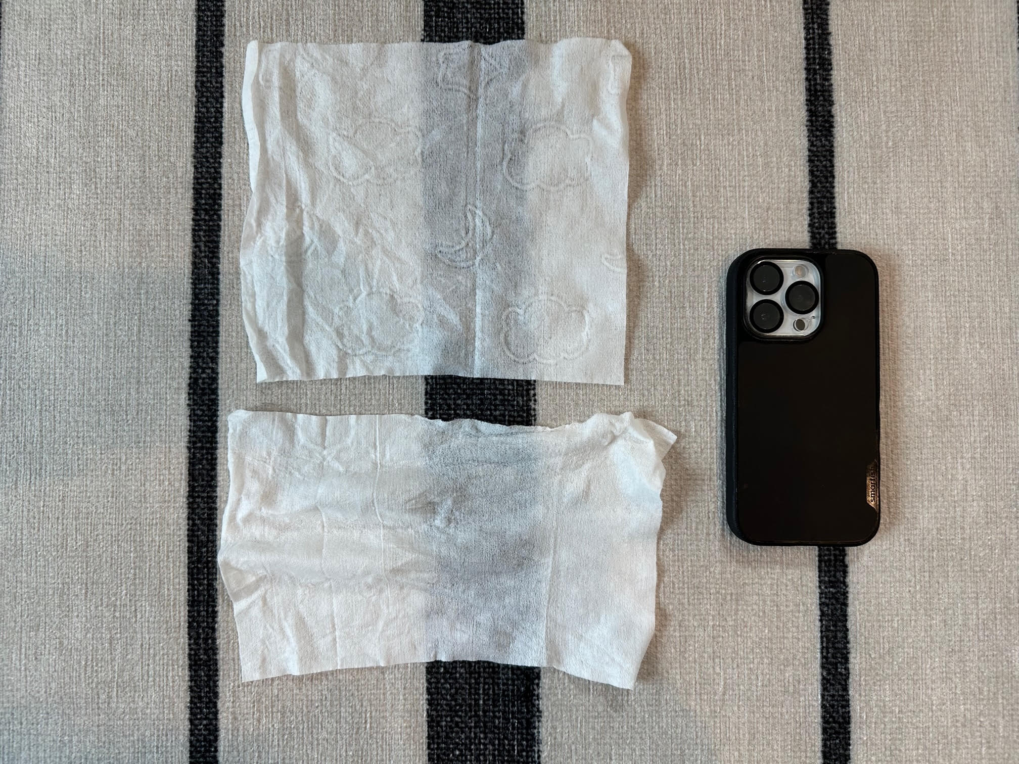 A Kirkland wipe next to a wipe by Eco by Naty, one of the smallest wipes I tested, with an iPhone 14 Pro tossed in for scale.