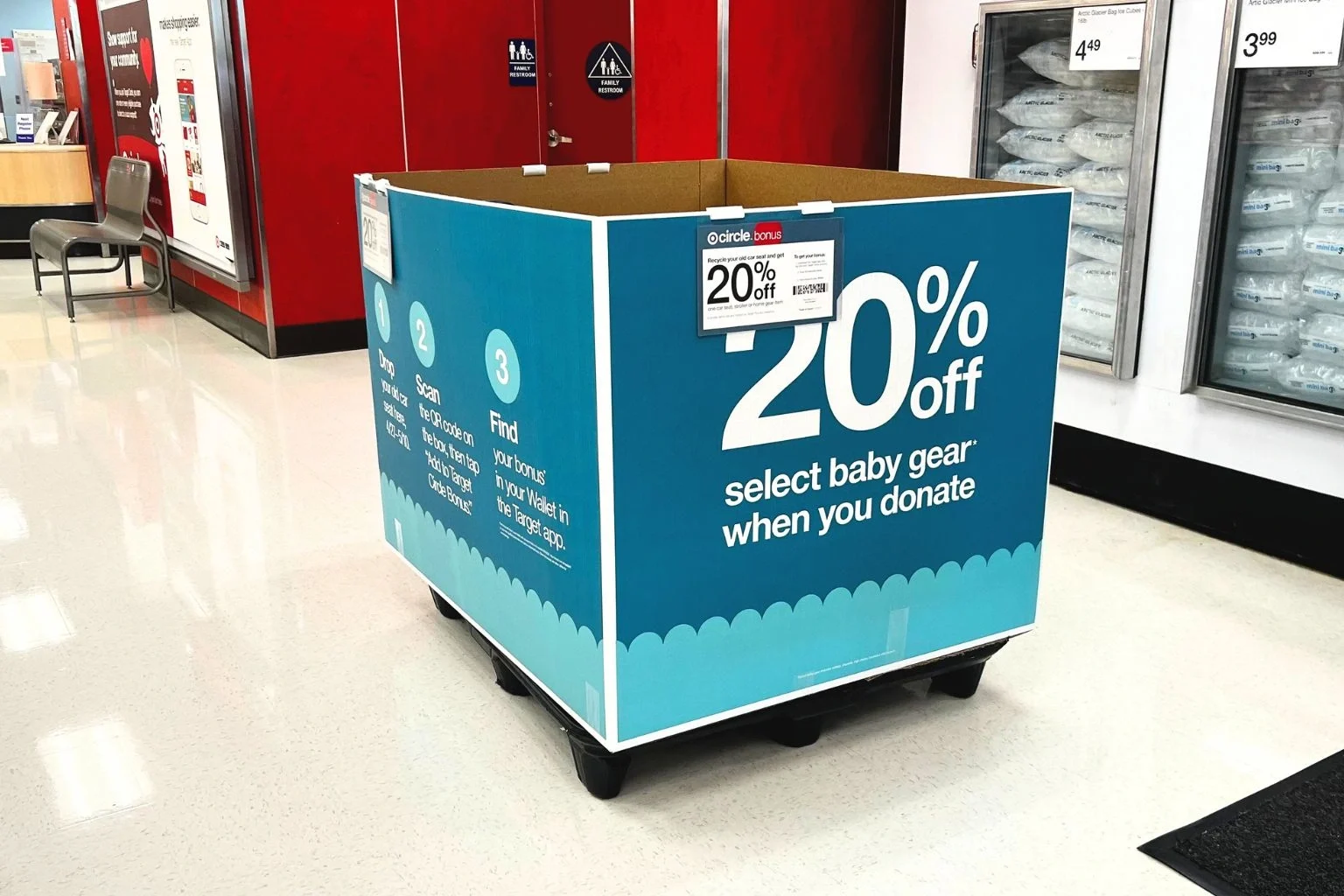 A large, blue cardboard box in a Target aisle that reads "20% off select baby gear when you donate" on the side.