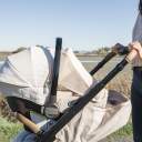 A woman's hands holding the handlebar of a Nuna Tavo stroller with a beige canopy with a Nuna Pipa urbn infant car seat attached to the top. thumbnail.