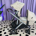 Side view of an UPPAbaby Vista V3 stroller with beige canopies in double mode, with a toddler seat in the top position and a bassinet in the lower position. thumbnail.