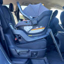 A side view of a black UPPAbaby Aria Lightweight Infant Car Seat installed in a vehicle. thumbnail.