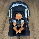 Front view of a small doll harnessed into a black Joie Mint Latch Infant Car Seat thumbnail.