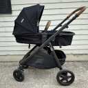 A black Joie Ginger stroller in bassinet mode against a beige background. thumbnail.