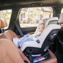 Toddler sitting rear-facing in a beige Nuna Rava Convertible Car Seat in a vehicle with tan seats. thumbnail.