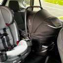 A grey Graco SlimFit3 LX 3-in-1 Convertible Car Seat installed in the center seat of a Toyota Rav4 next to a black Nuna Pipa Aire with the canopy up. thumbnail.