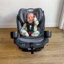 A two-month-old baby with light skin buckled into the Graco SlimFit3 LX 3-in-1 Convertible Car Seat. The car seat is not installed in a vehicle, it's resting on a light wooden floor. thumbnail.