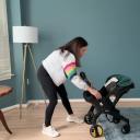 A woman in a gray sweatshirt and black leggings transforms a Doona car seat with a green canopy from stroller mode to car seat mode. thumbnail.